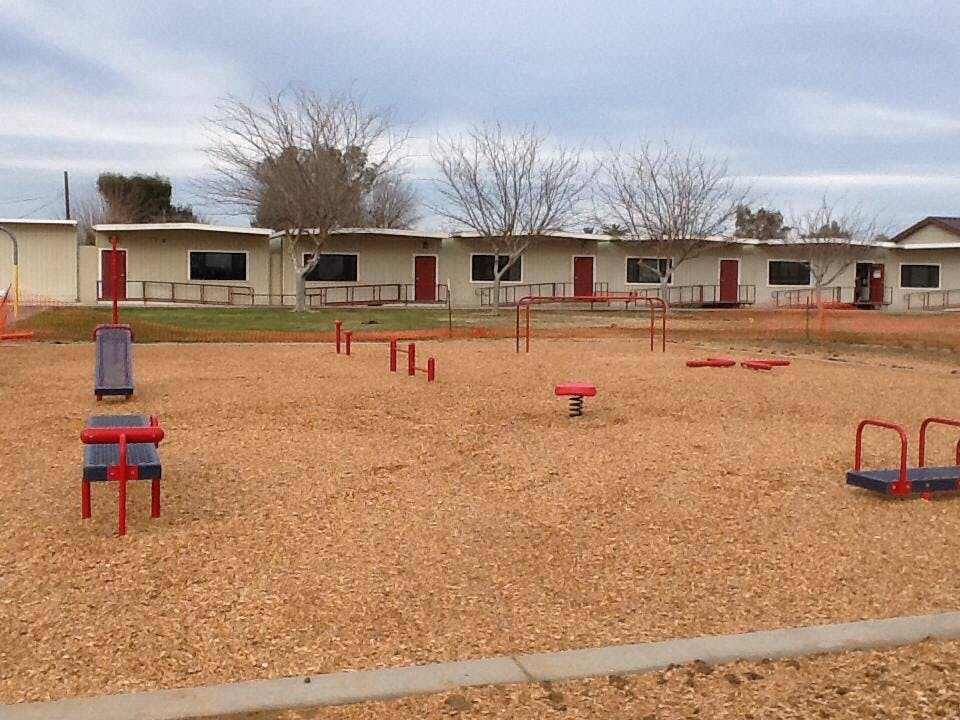 Playground with wood chips and various play equipment in front of buildings