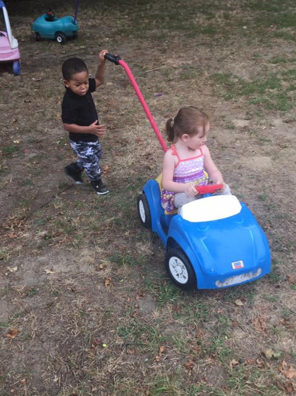 Child pushing another child in a blue toy car