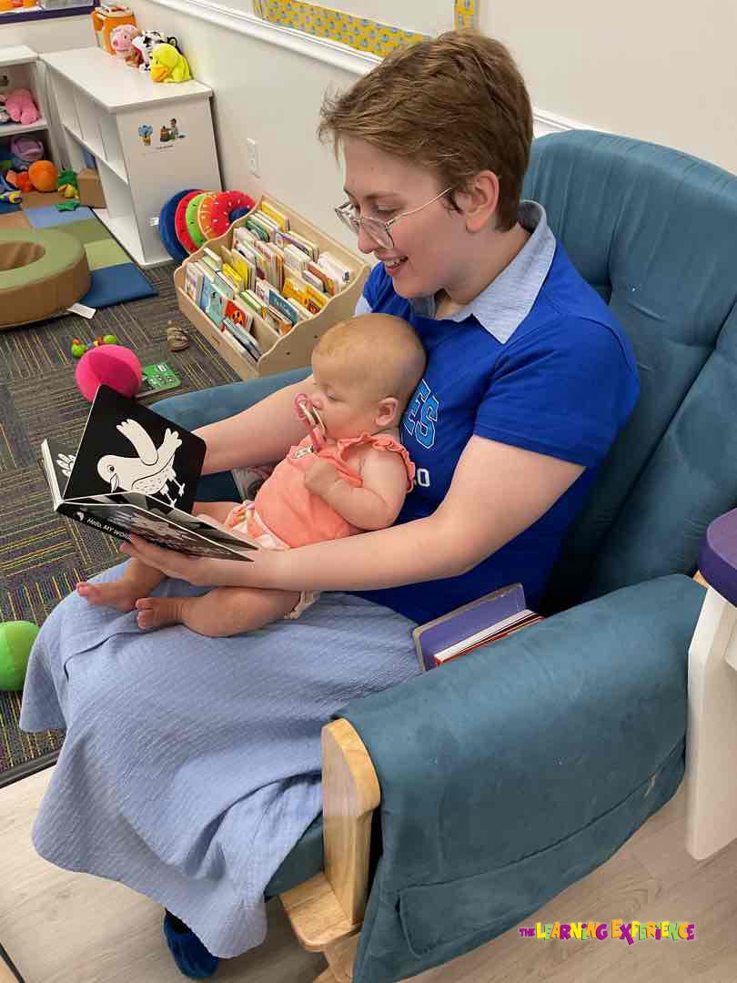 Person sitting in a chair holding a child and reading a book
