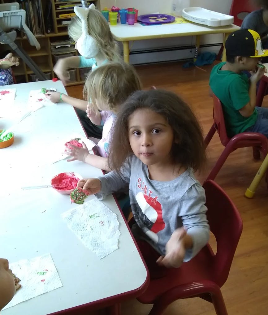 Child at a table holding a decorated cookie, other children nearby