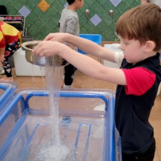 Child pouring water from a metal bowl into a clear bin