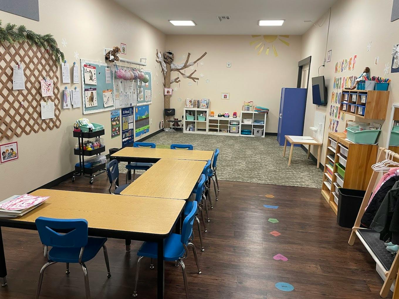 Empty classroom with light wooden tables and blue chairs, educational decorations