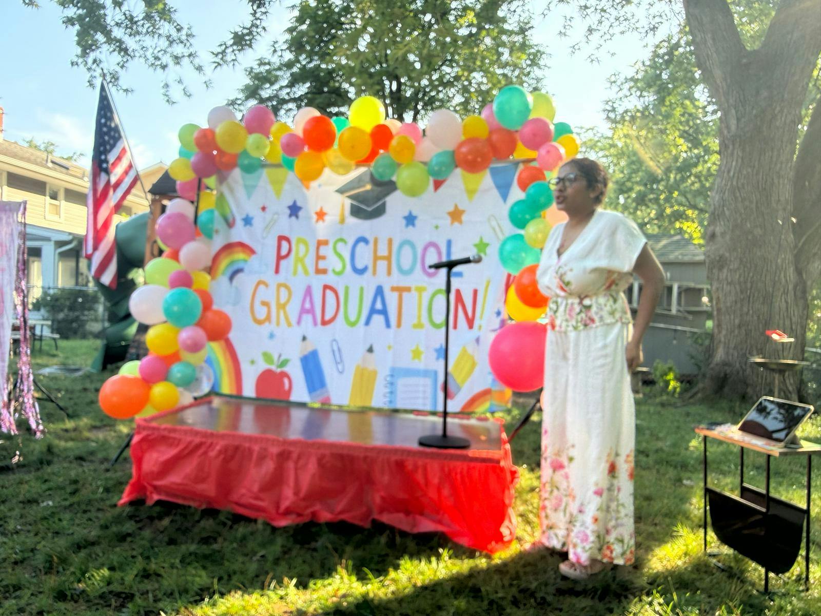 Person standing at a microphone in front of a preschool graduation backdrop