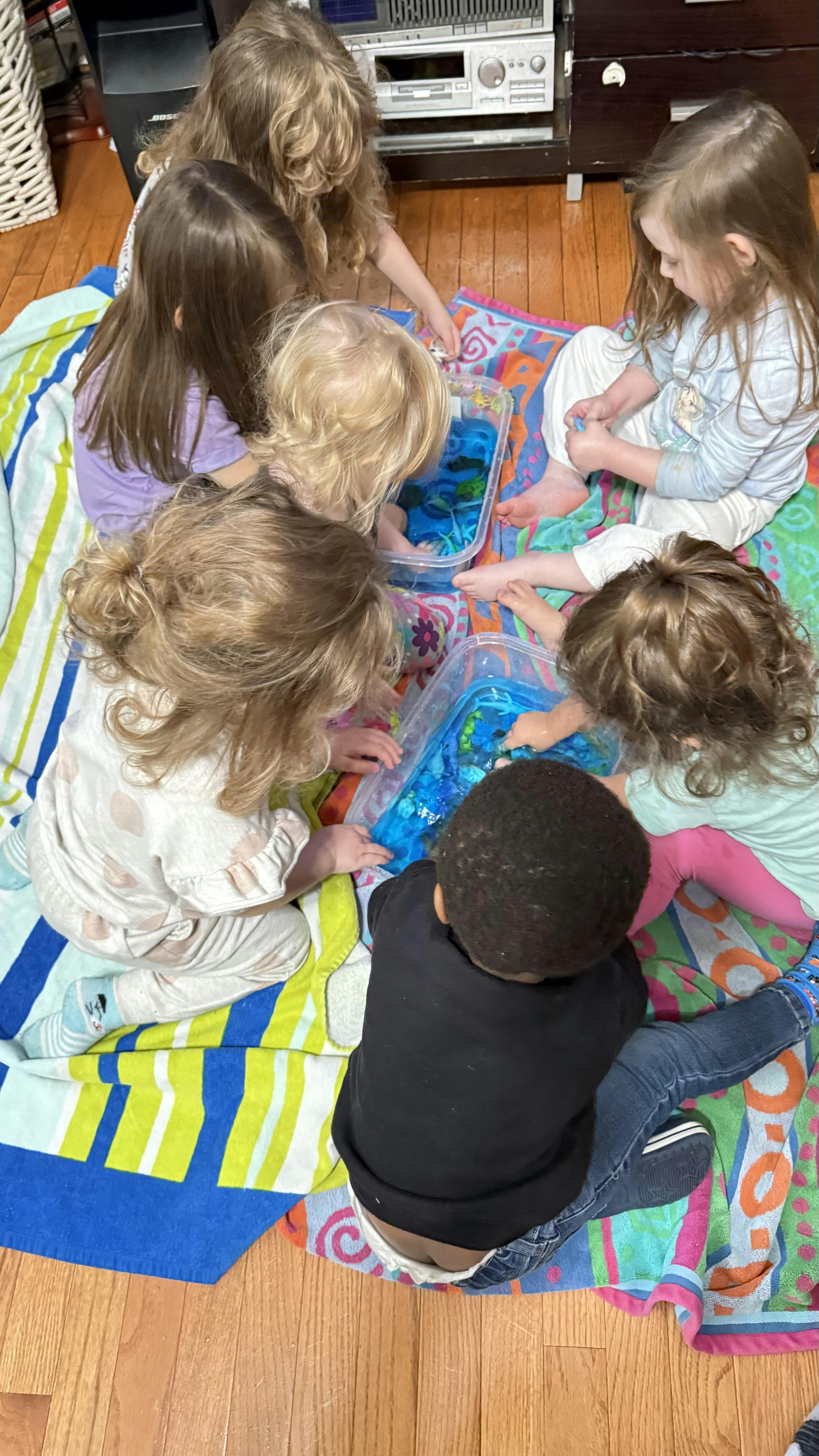 Group of children sitting on blankets playing with blue sensory bins