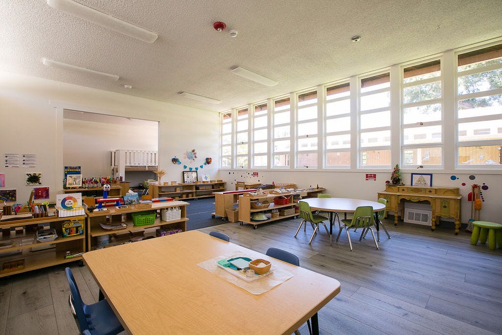 Empty classroom with small tables and chairs, shelves with learning materials