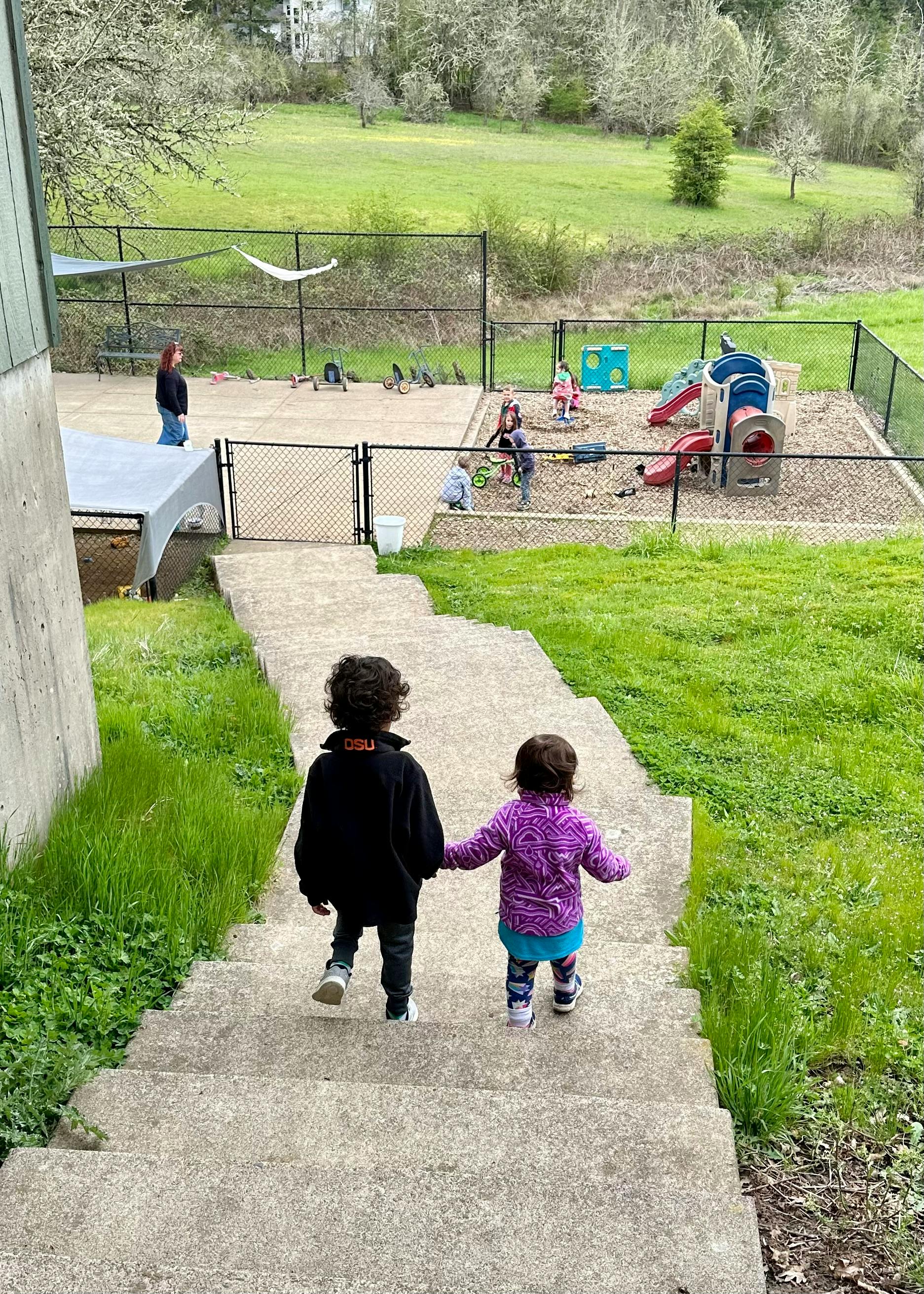 Two children holding hands walking down stairs towards a playground