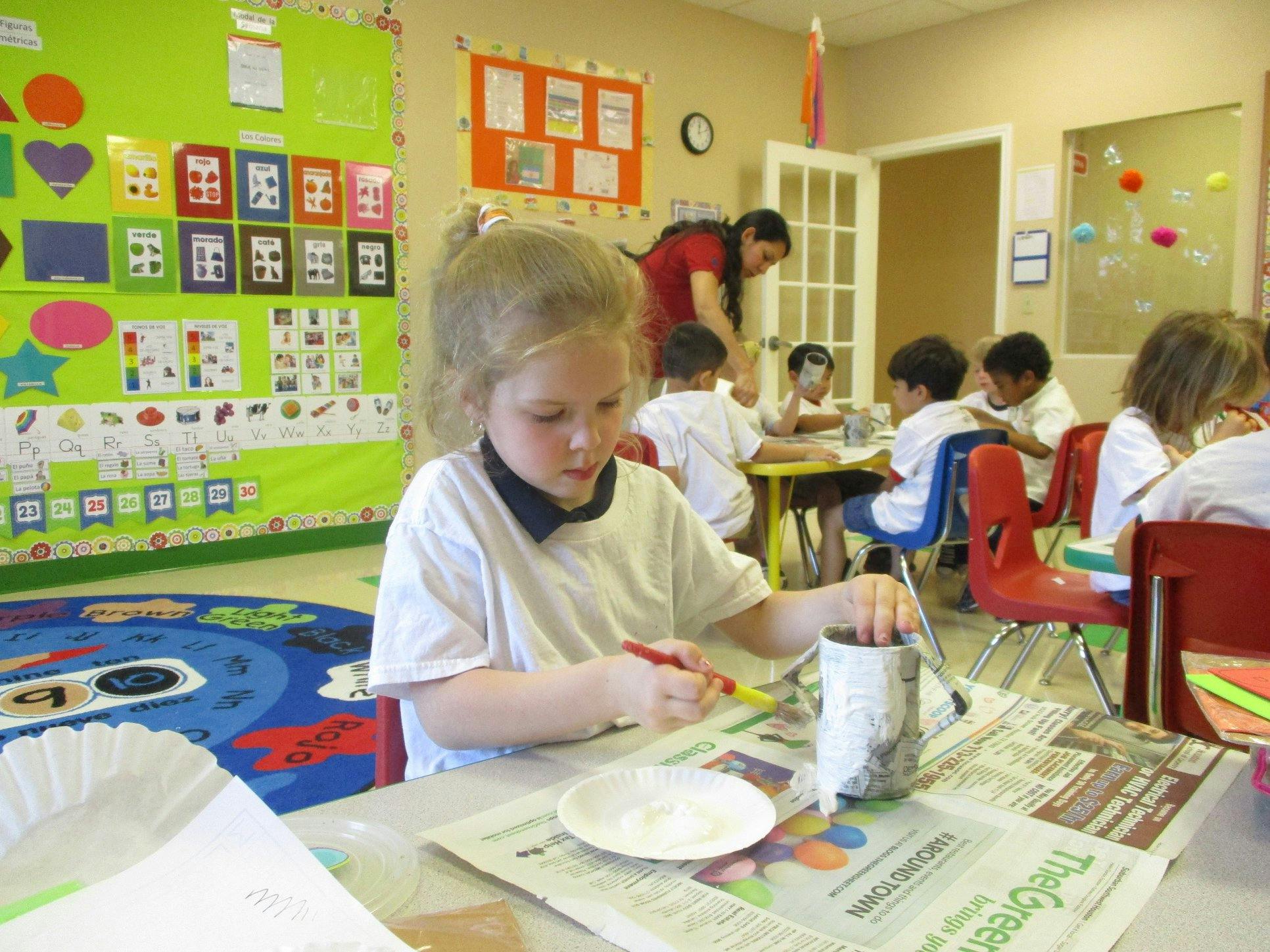 Child painting a craft project at a table in a classroom