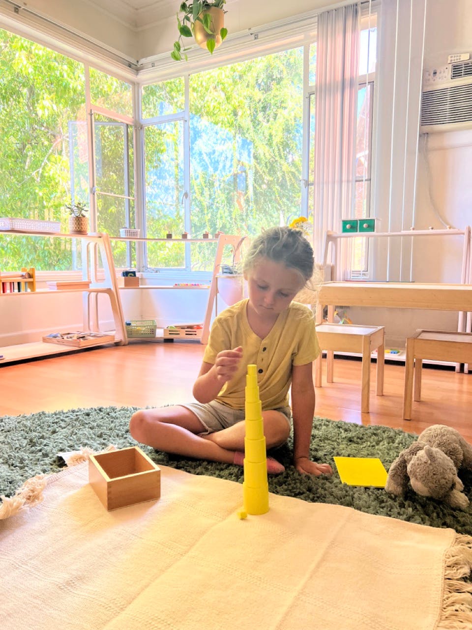 Child sitting on a rug, looking at a yellow conical tower