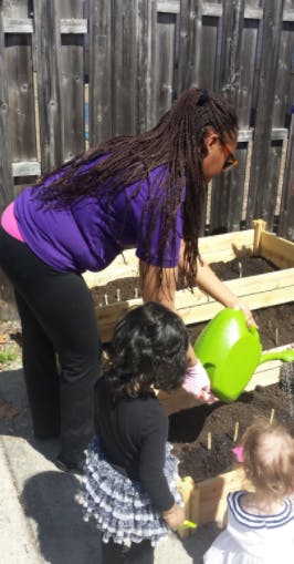 Person watering a garden bed with two children watching
