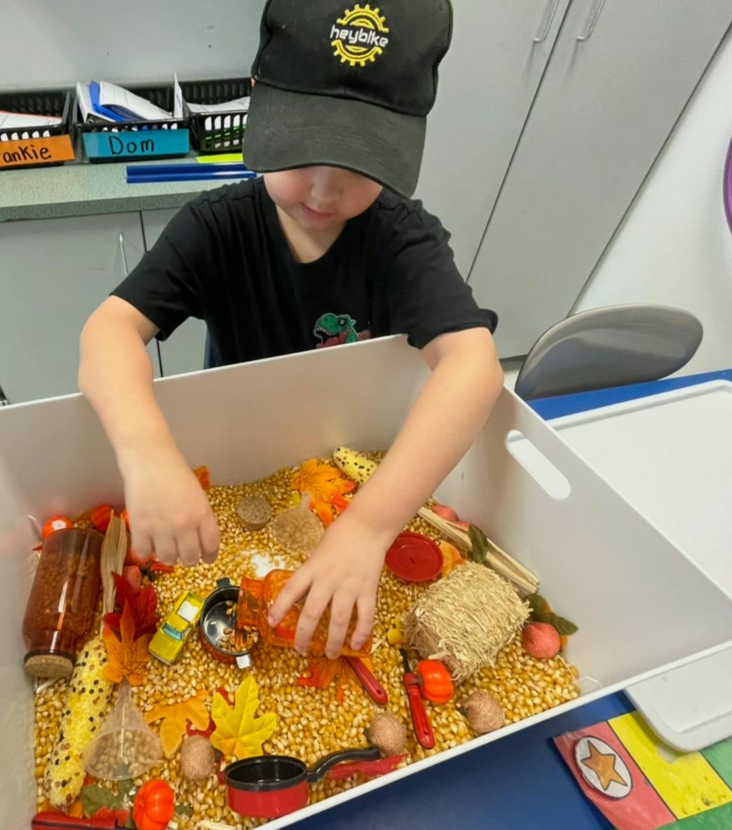 Child playing with corn kernels and small objects in a bin