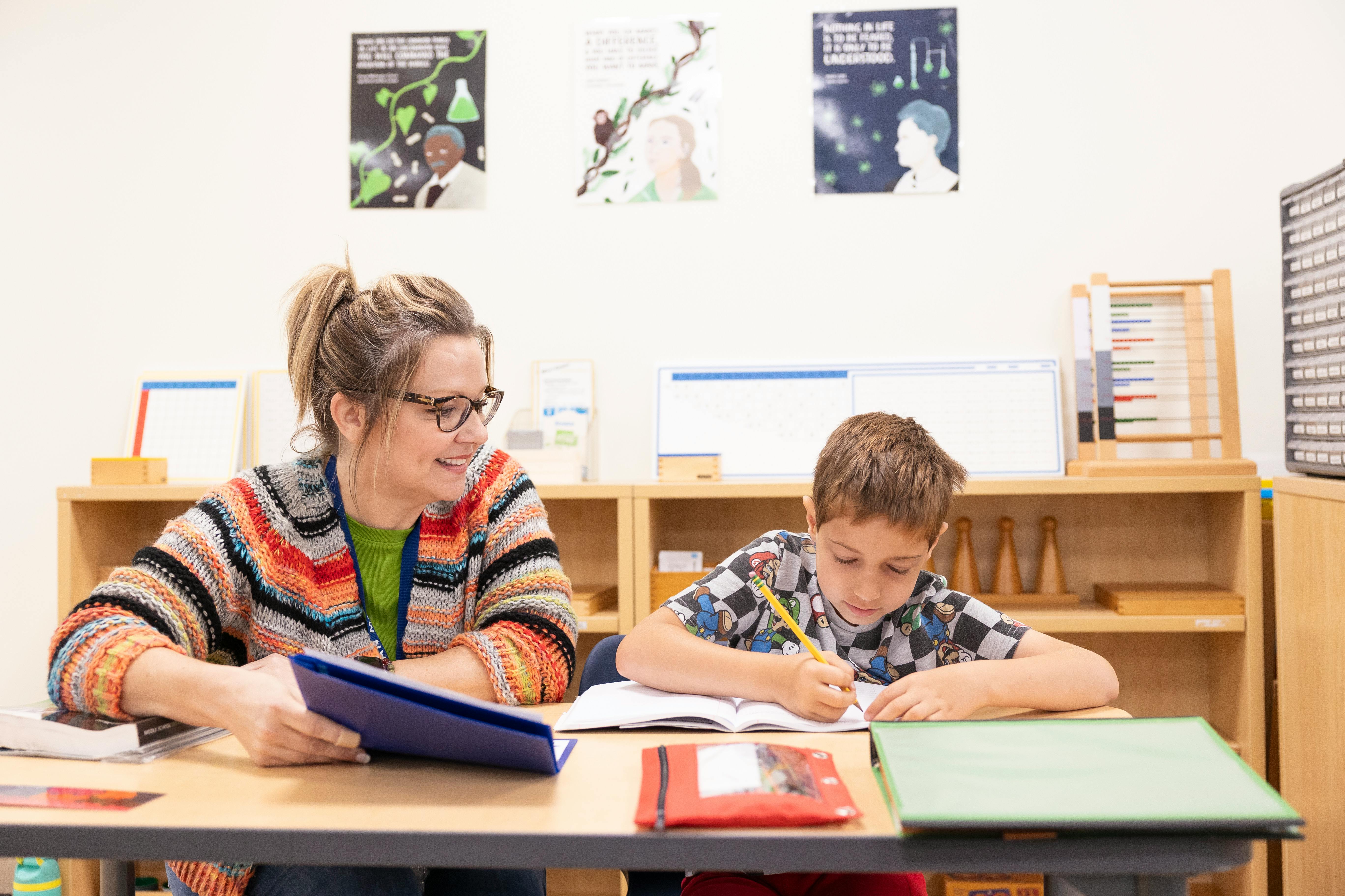 Adult and child sitting at a desk, child writing in a book