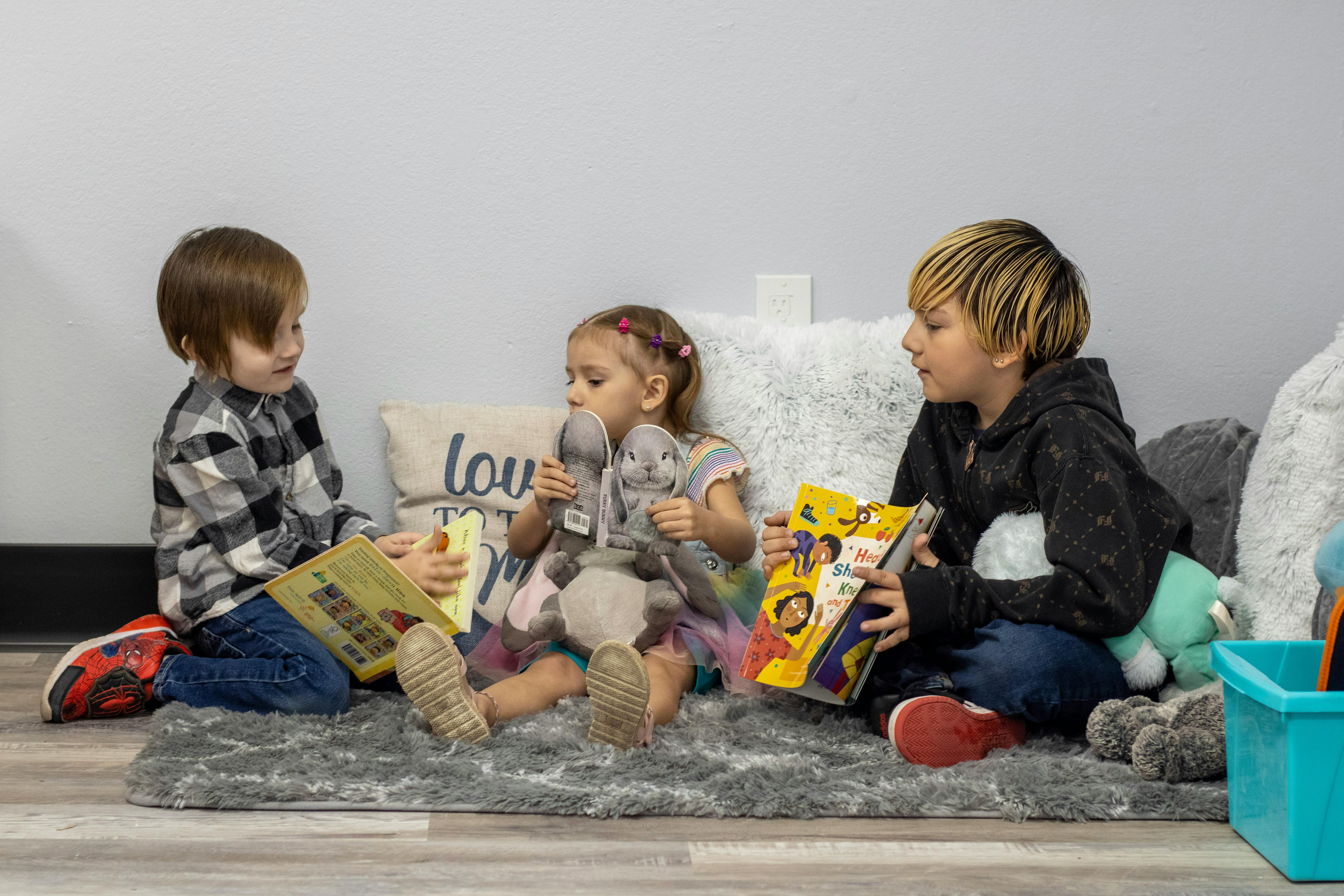 Three children sitting on a rug, two reading books