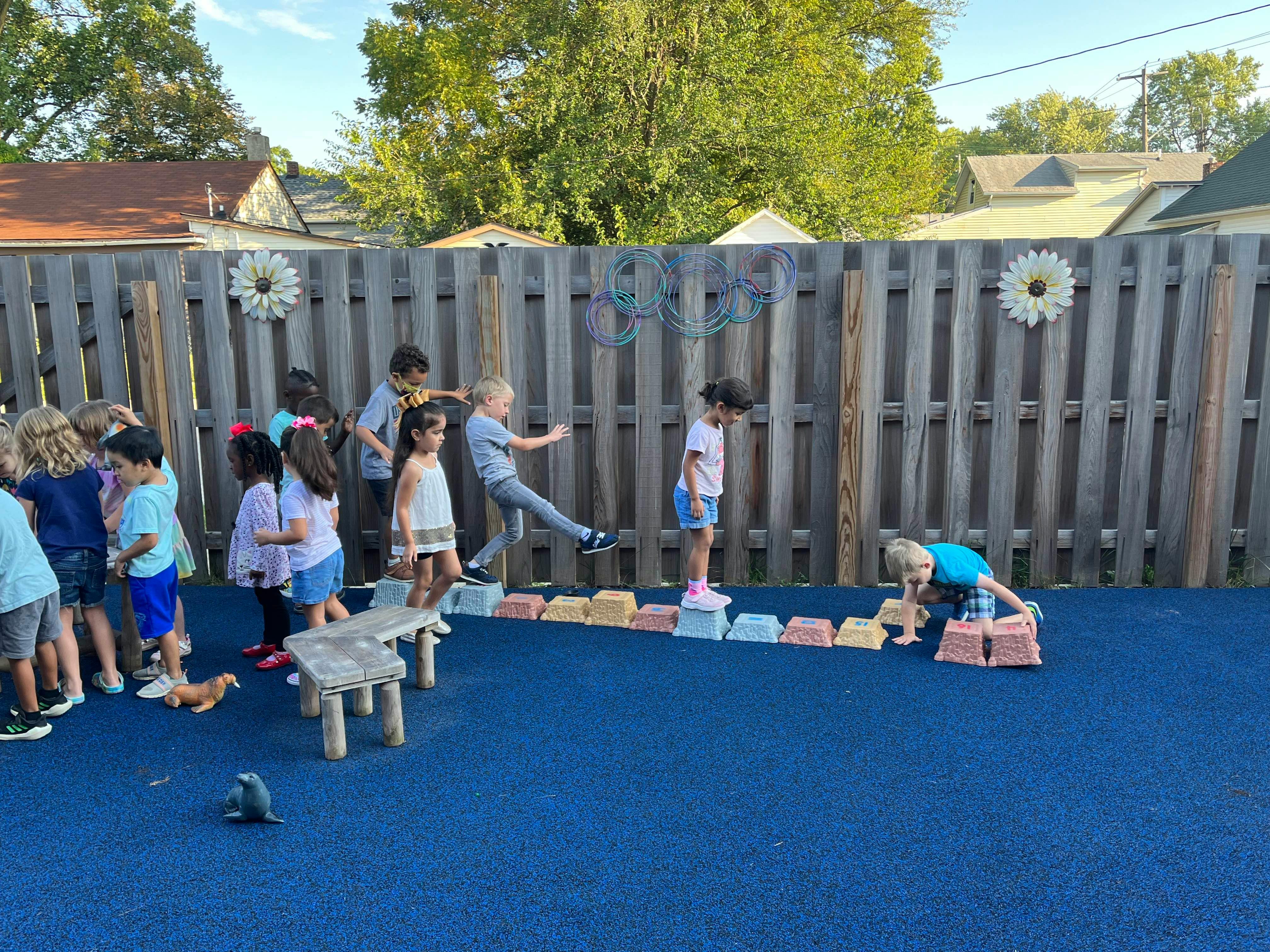 Children playing on a blue surface next to a wooden fence