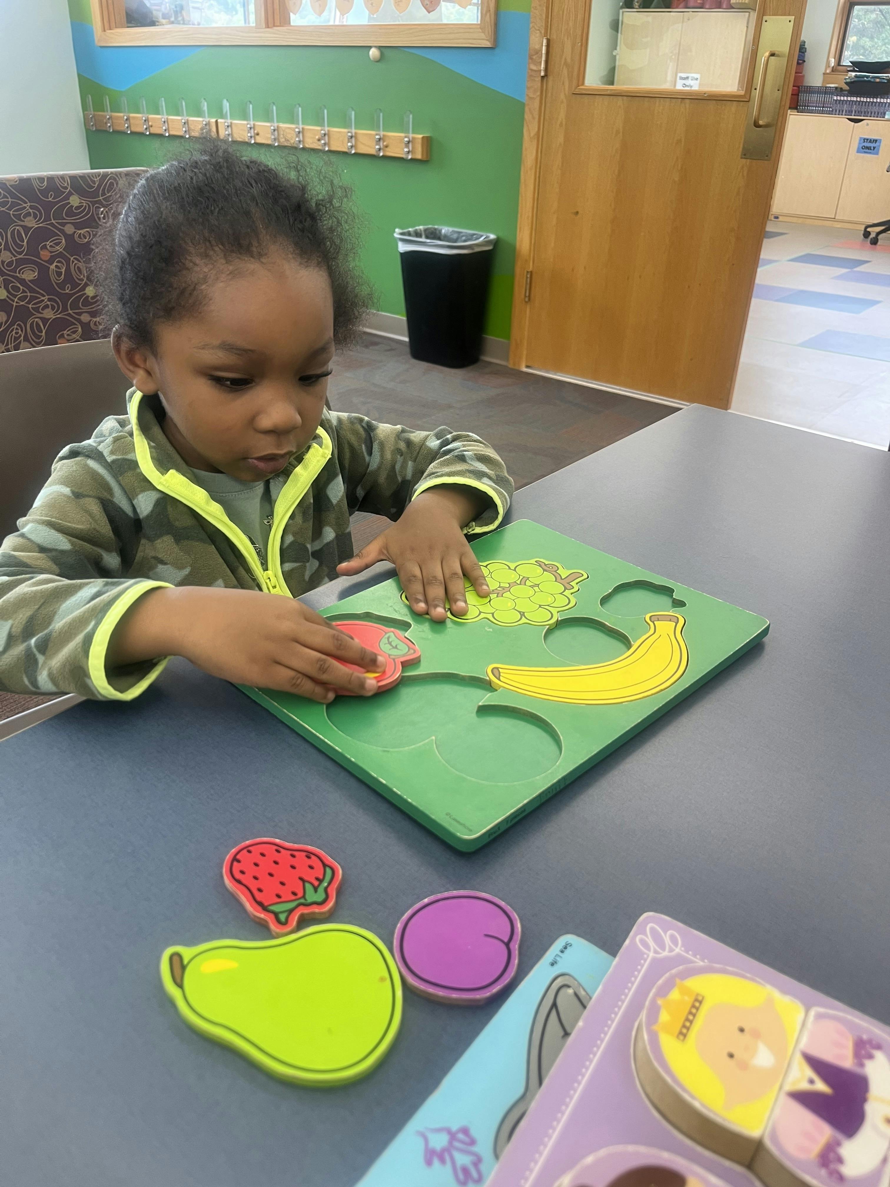 Child playing with a fruit puzzle in a classroom