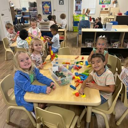Children sitting at tables playing with plastic building blocks in a classroom