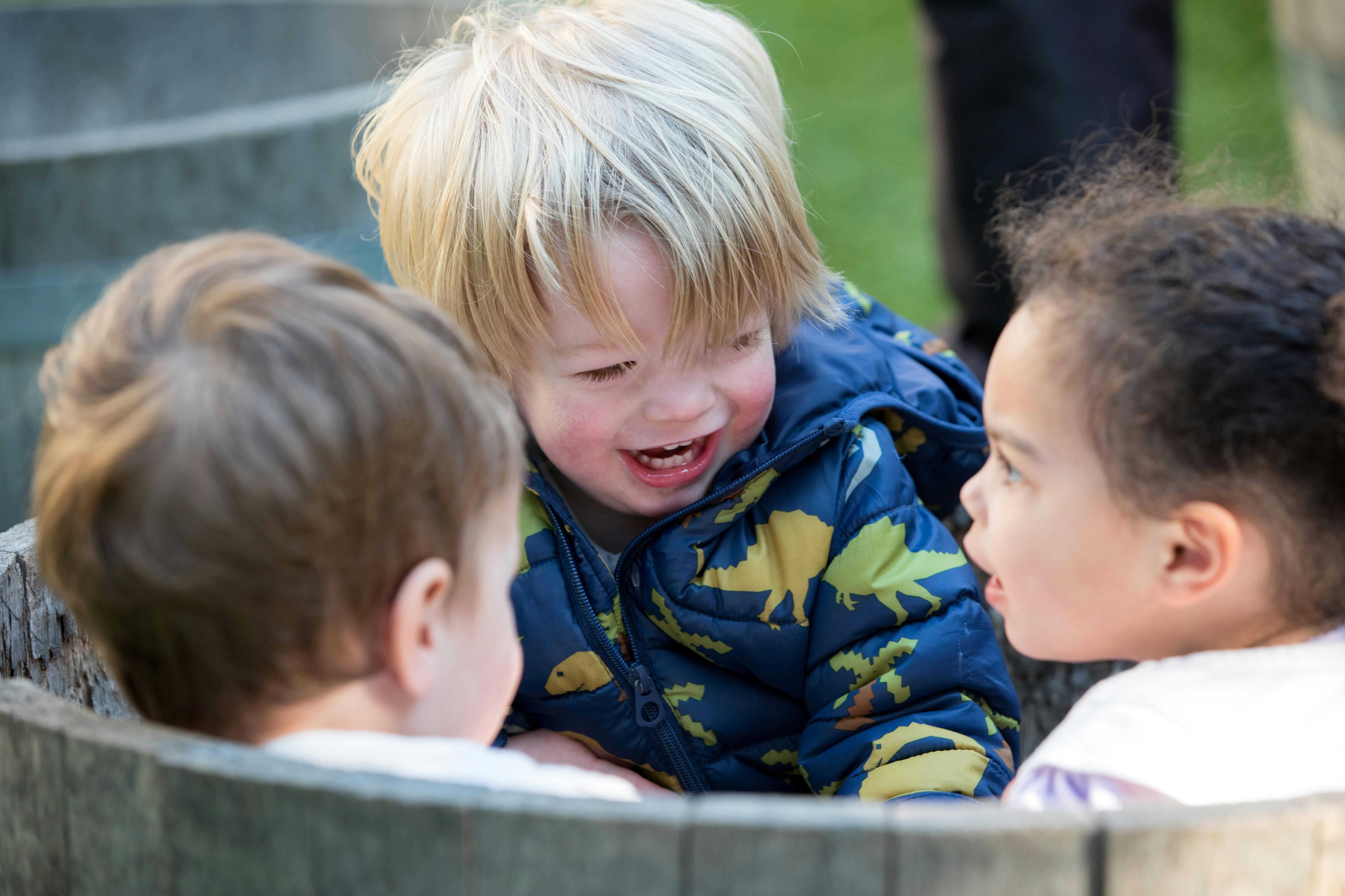 Three children looking at each other in a wooden barrel