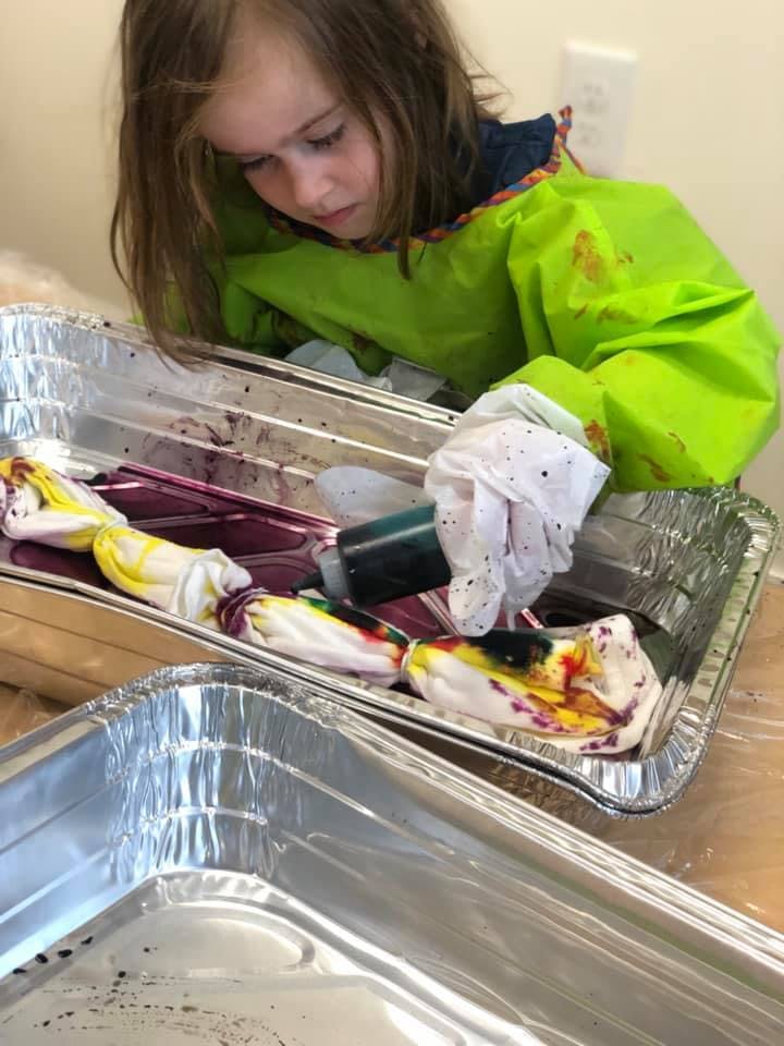 Child in a green smock tie-dyeing fabric in a foil pan