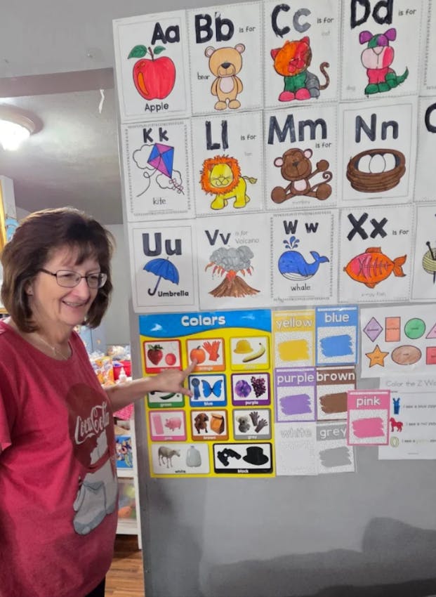 Person pointing at a color chart with alphabet cards on a wall
