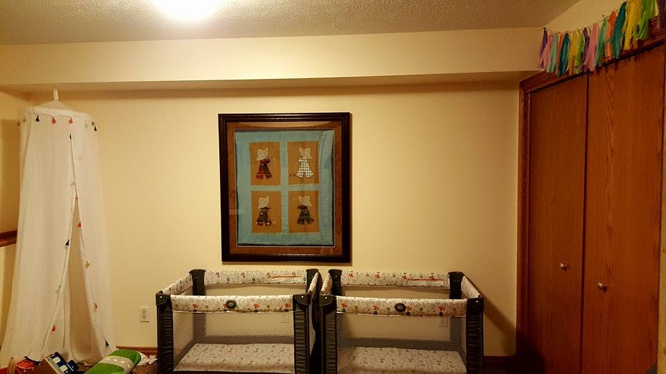 Two cribs in a room with a framed picture on the wall