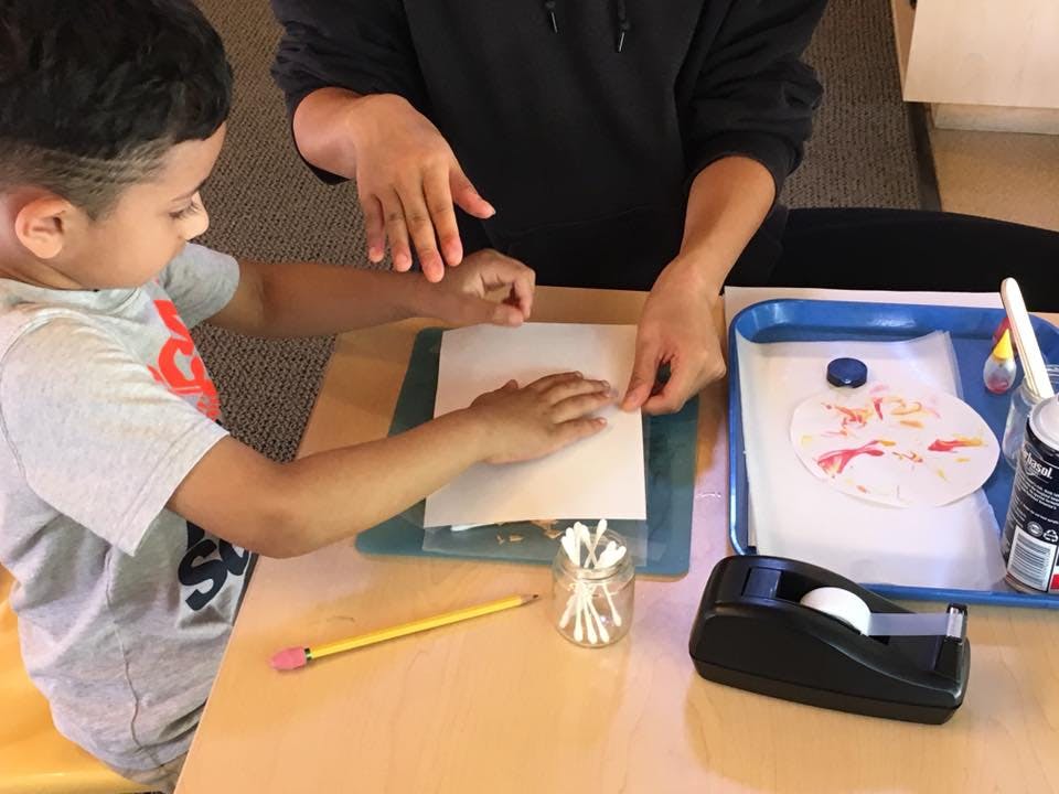 Child and person working on paper craft at a table