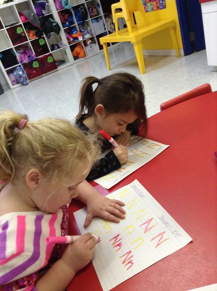 Two children writing on paper with markers in a classroom