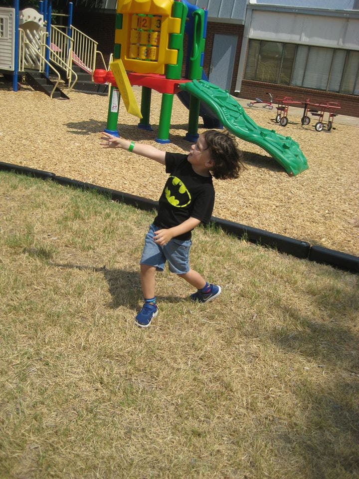 Child in a Batman shirt reaching out on a playground