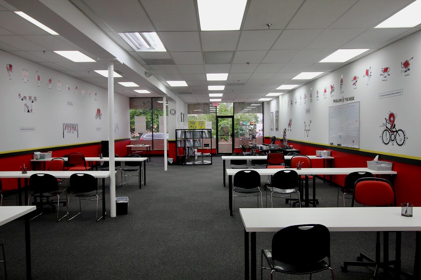 Classroom with multiple white tables and chairs, whiteboards, and red and yellow accents