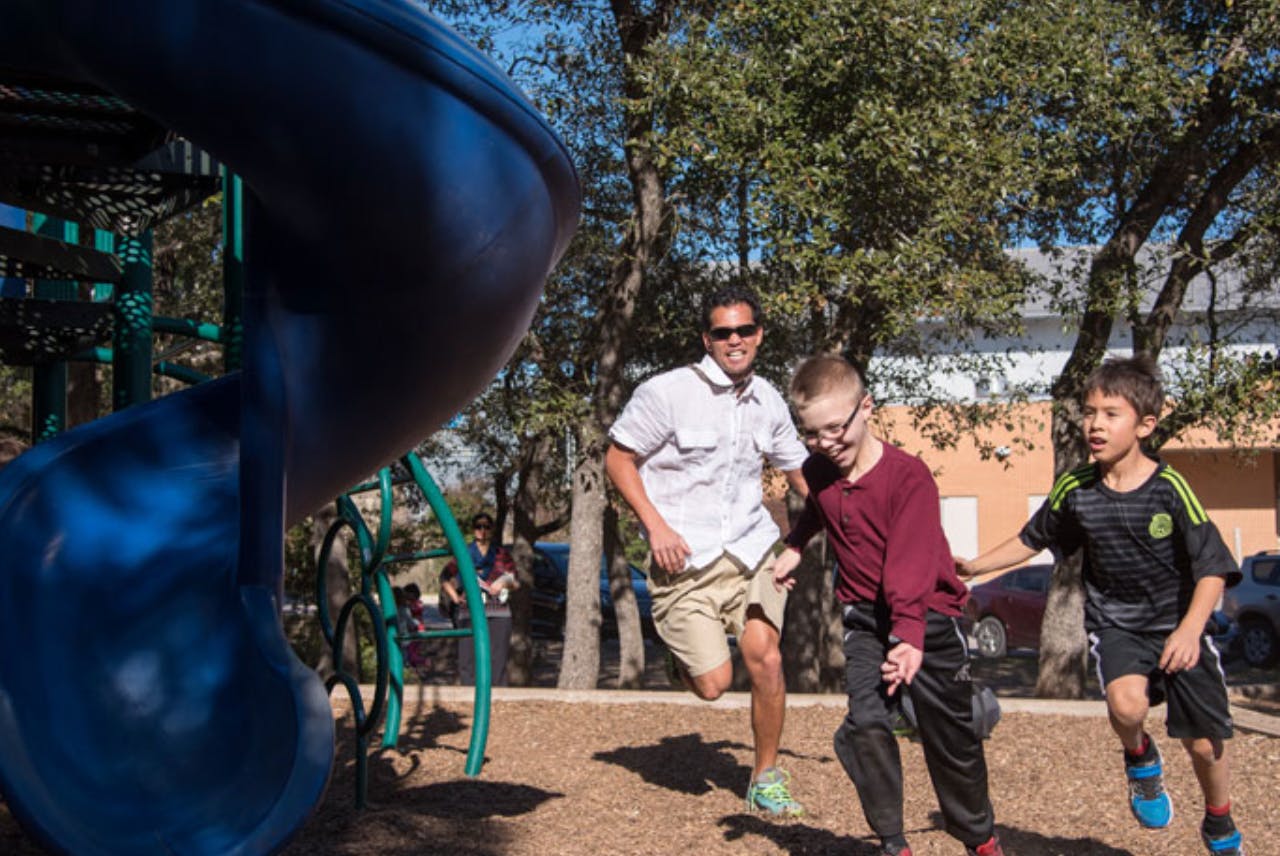 Adult and two children running on a playground
