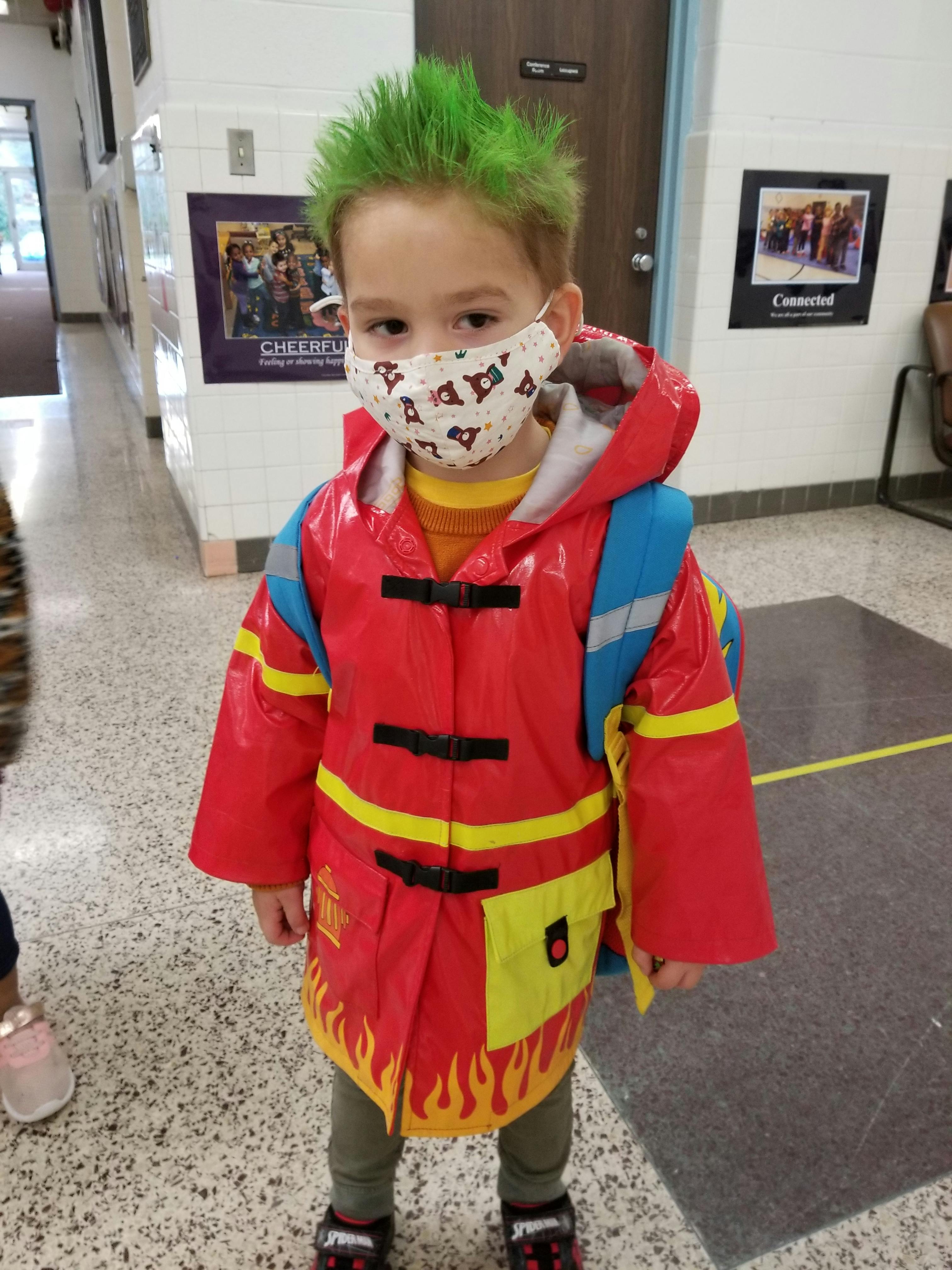 Child with green hair and face mask wearing a firefighter costume