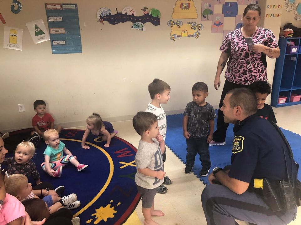 Police officer kneeling and talking to children in a classroom with an adult supervising