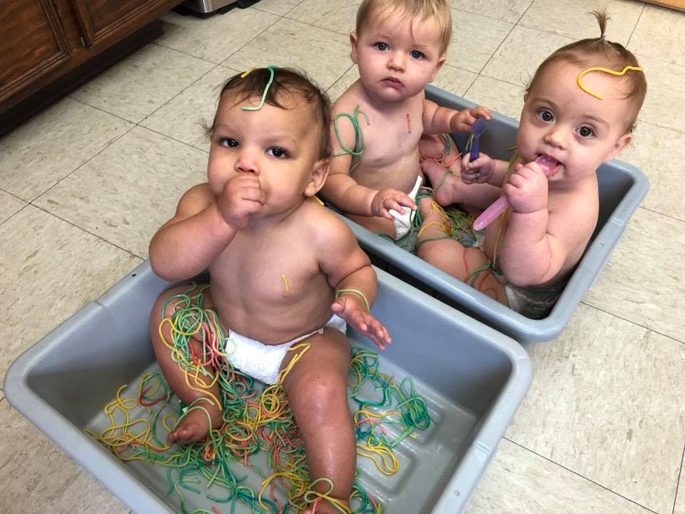 Three babies sitting in tubs with colorful rubber bands