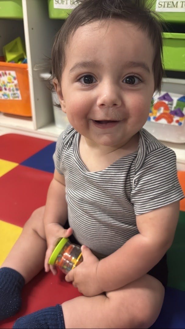 Child in a striped shirt sitting on a colorful mat holding a rattle