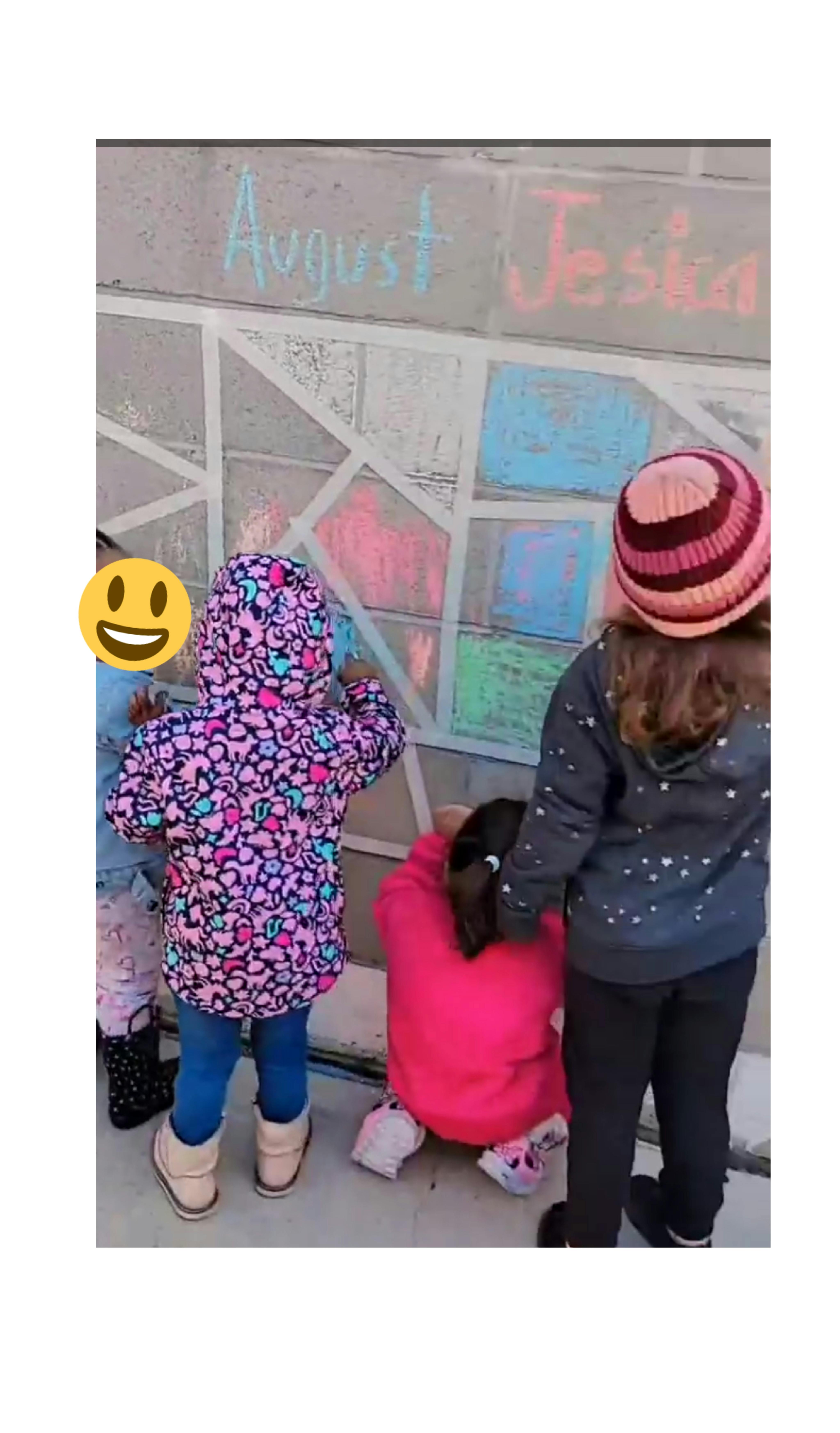 Children drawing with chalk on a wall with names "August" and "Jessica"