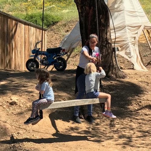Person helping two children on a wooden swing