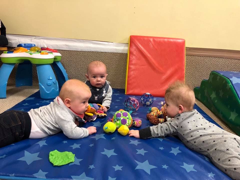 Three babies playing with toys on a blue mat