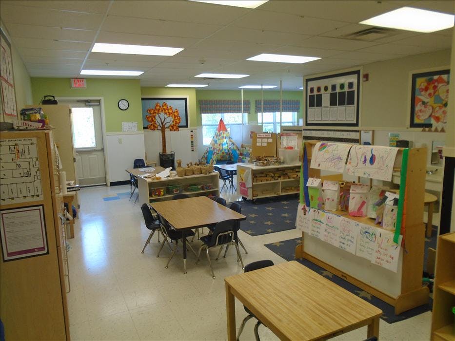 Classroom with child-sized tables and chairs, shelves, and a play teepee