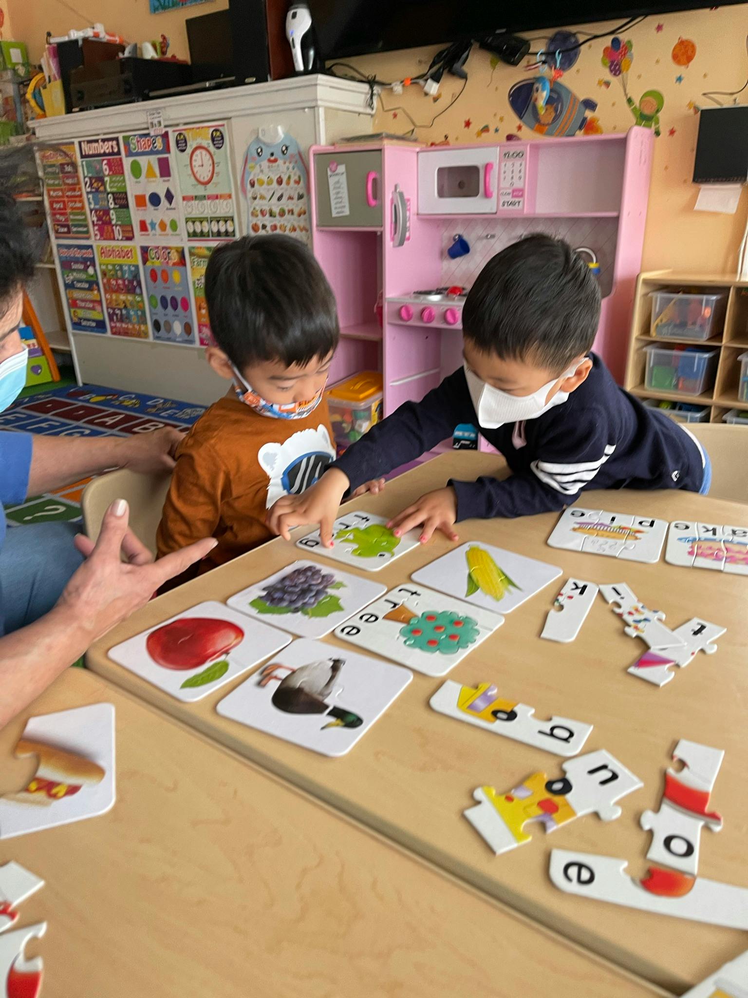 Two children and an adult playing with learning cards and puzzles at a table