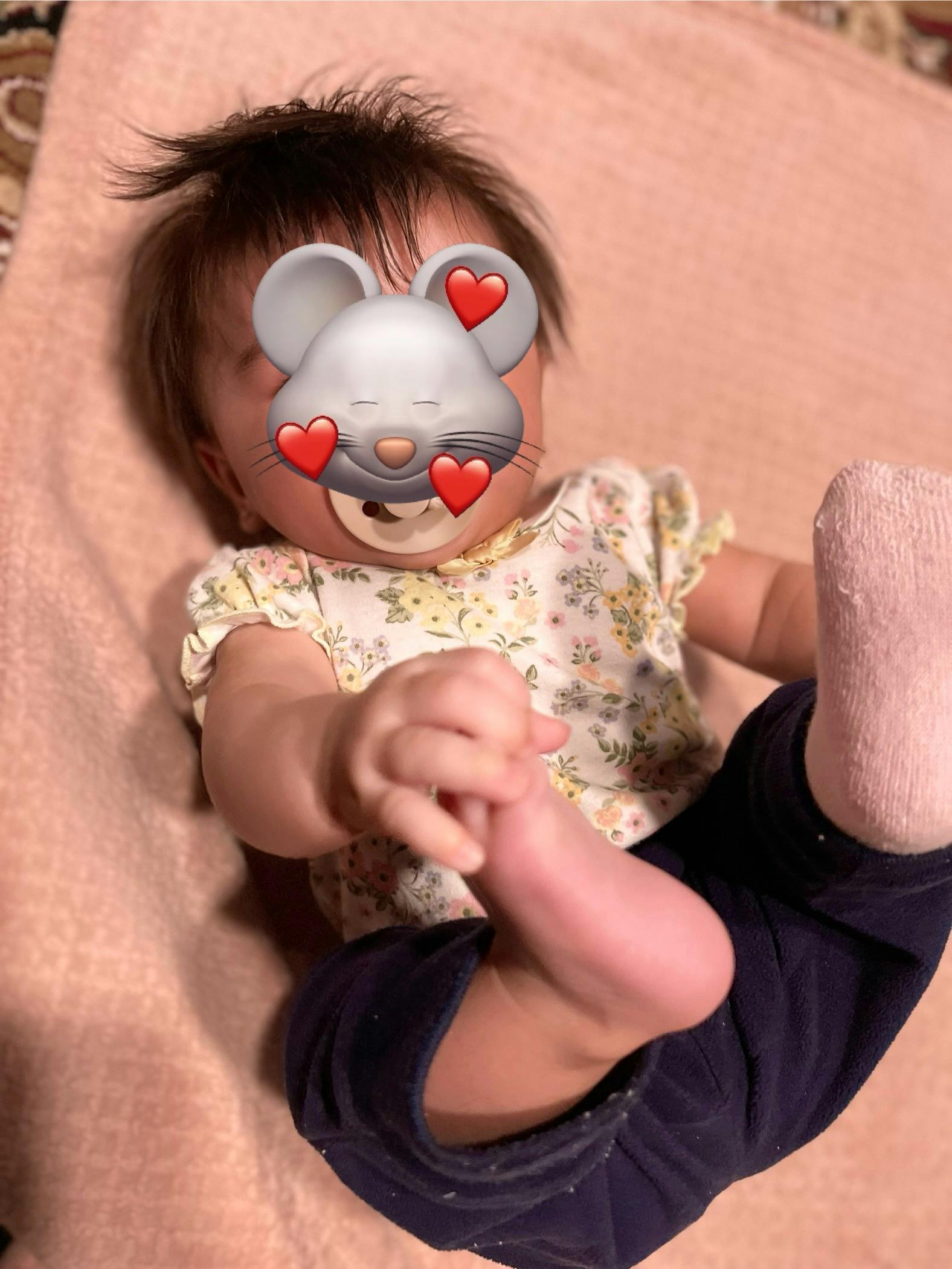 Child lying down with a pacifier, holding their foot