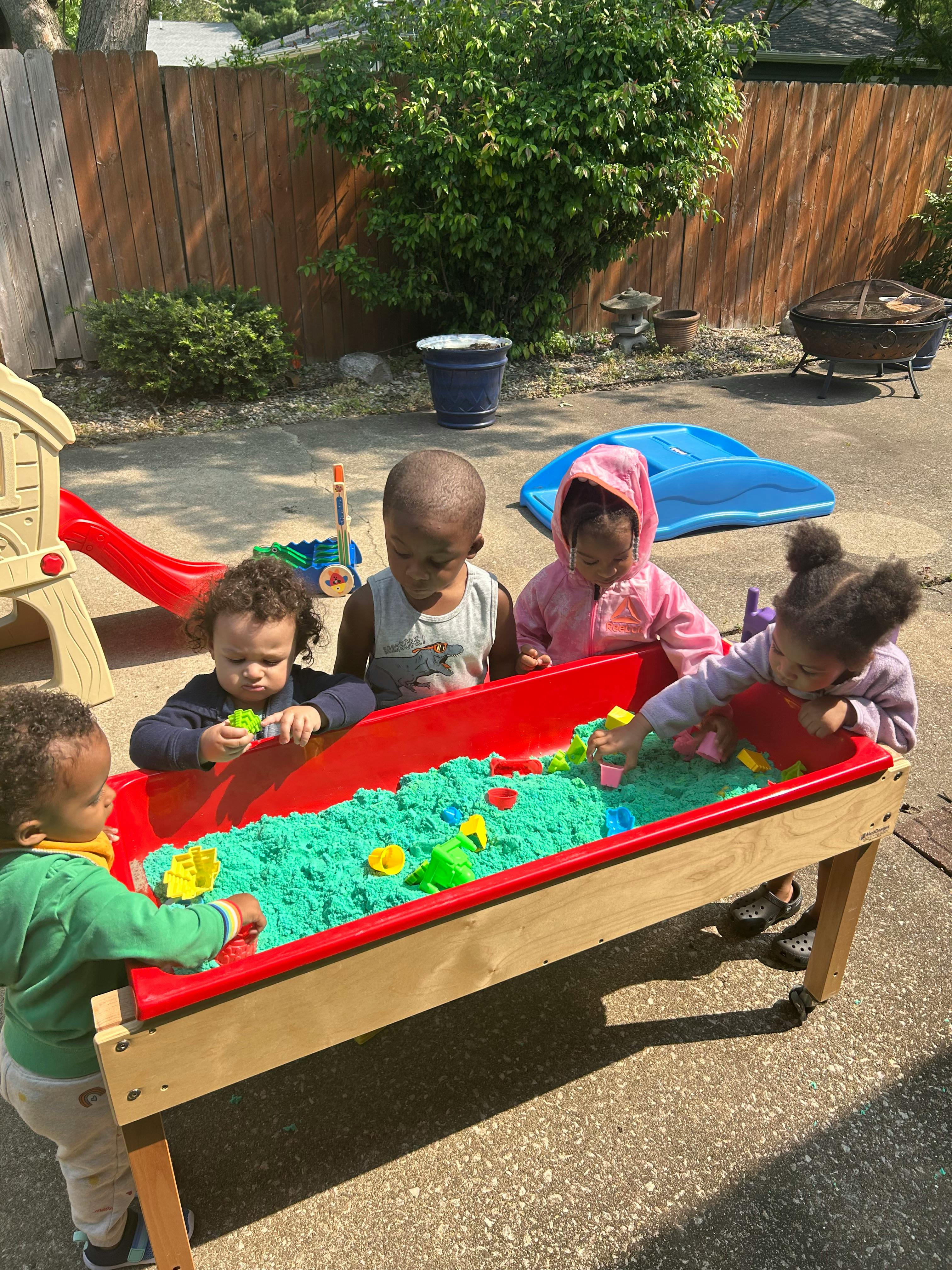 Children playing with kinetic sand in a red sand table outdoors
