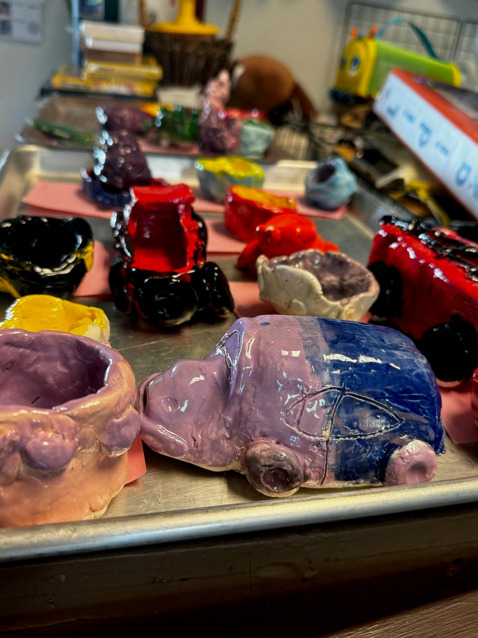 Glazed ceramic art pieces on a tray, including a purple and blue turtle