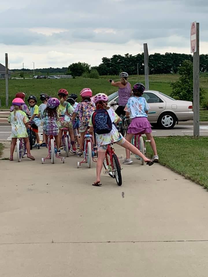 Group of children on bicycles with an adult standing by a car