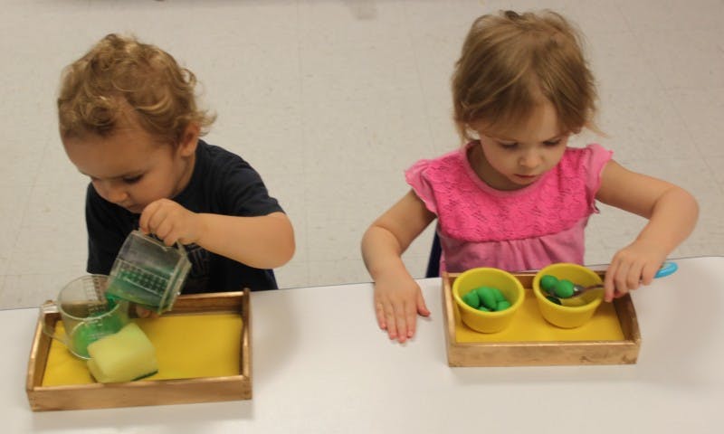 Two children playing with green liquid and green playdough at a table