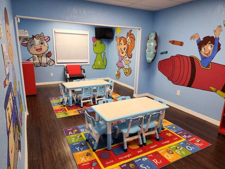 Small tables and chairs for children in a room with cartoon wall murals