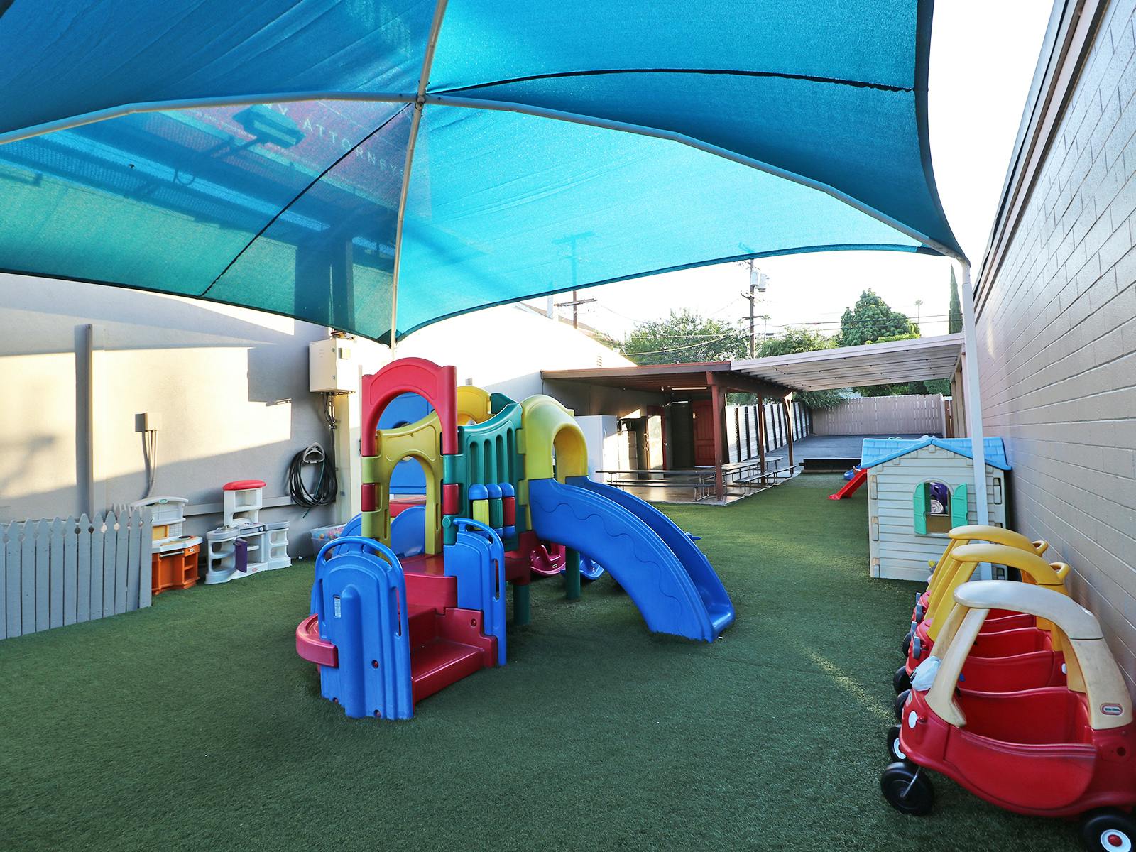 Colorful playground with slide, playhouse, and ride-on toys under a blue canopy