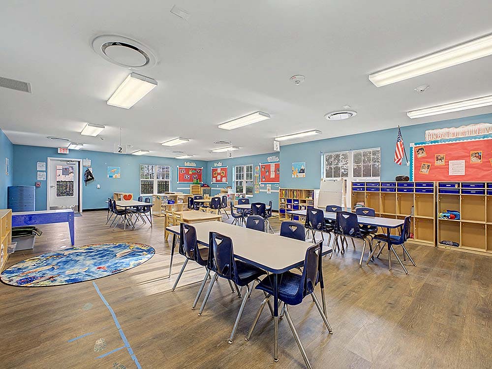 Classroom with small tables and chairs arranged, blue walls, and windows