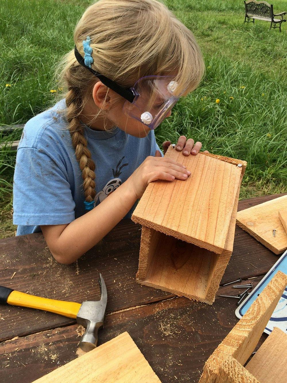 Child in safety goggles assembling a wooden birdhouse