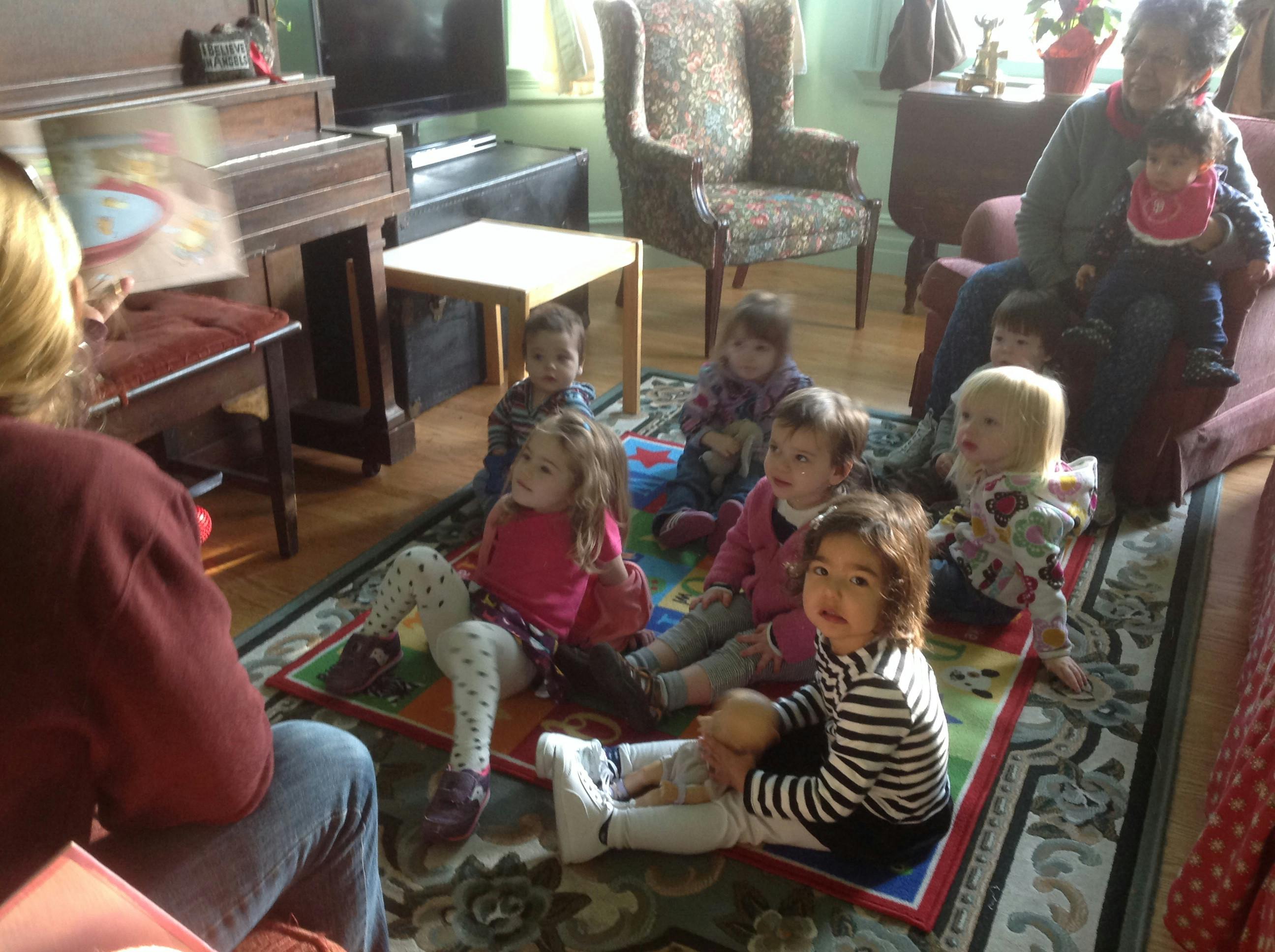 Person reading a book to a group of children sitting on a rug