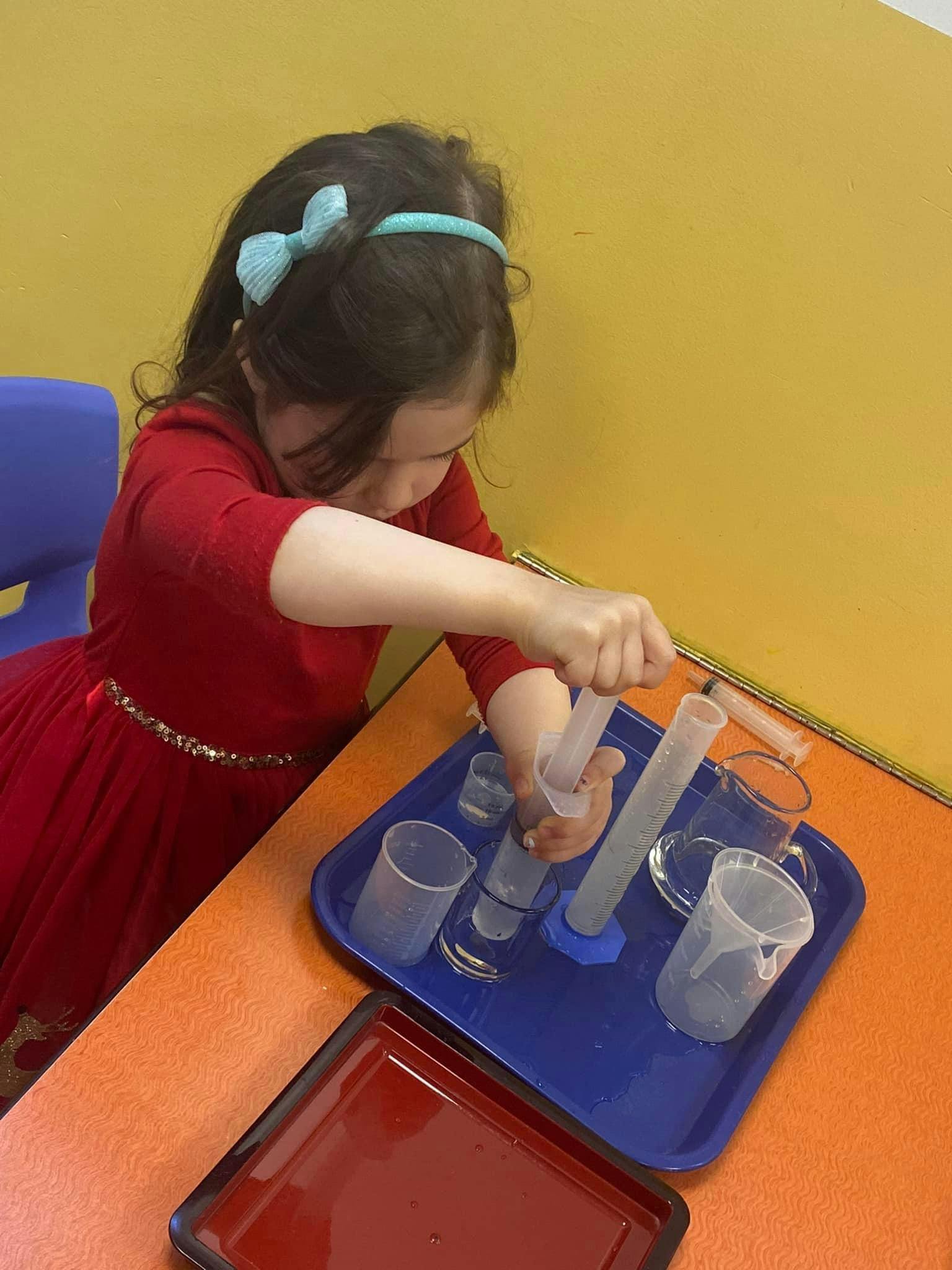 Child using a syringe with beakers and cylinders on a tray