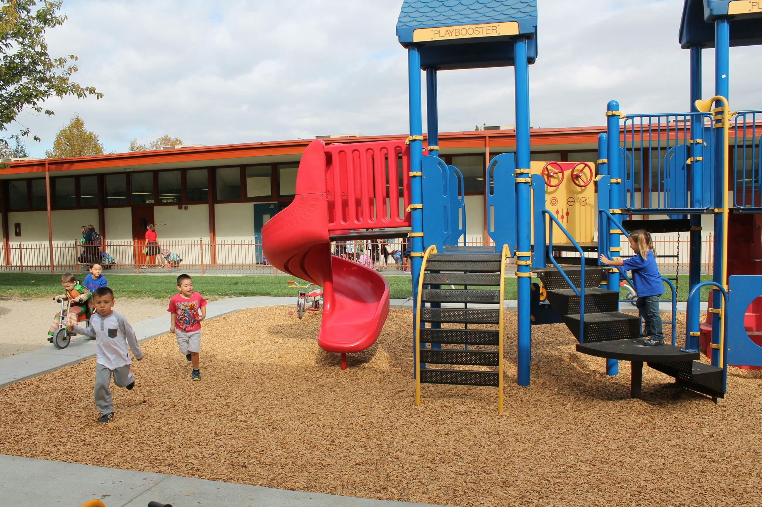 Children playing on a playground with a red slide and blue climbing structure