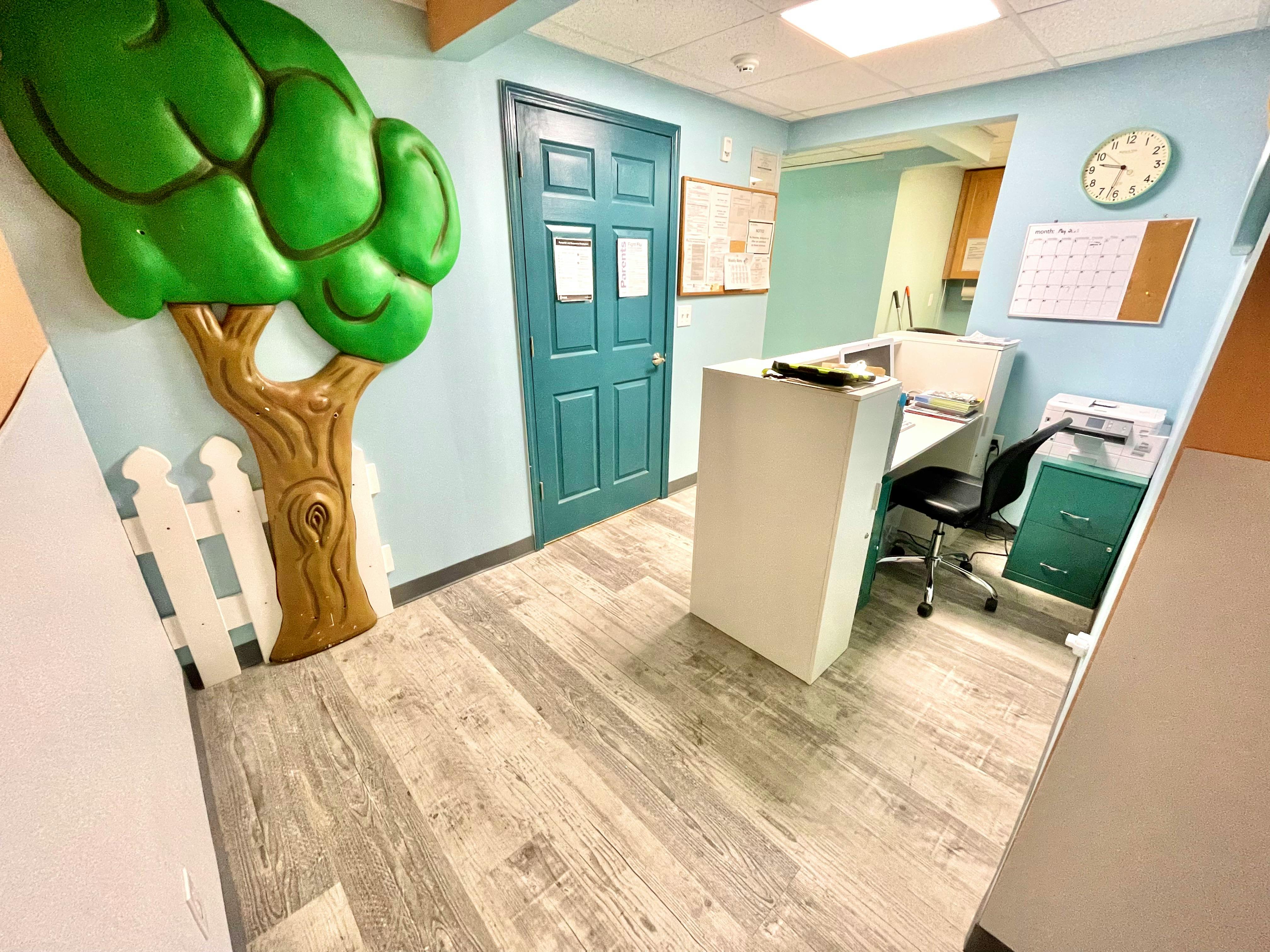 Reception area with a white desk, chair, and a decorative tree on the wall